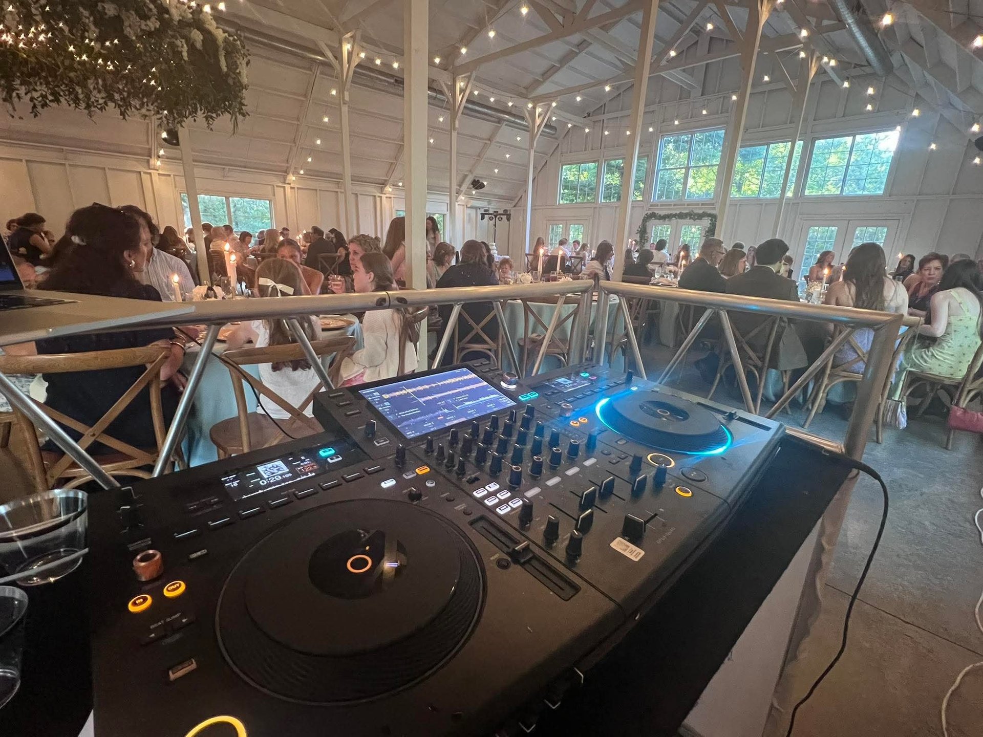 DJ turntables and mixer at an indoor event with guests dancing on a wooden deck under string lights