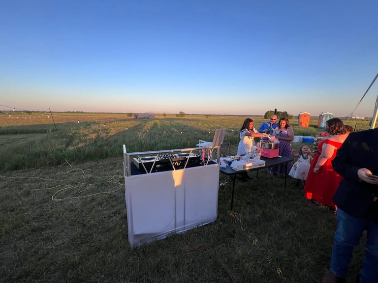 Group gathered around white cooler at outdoor event in field at dusk with clear sky