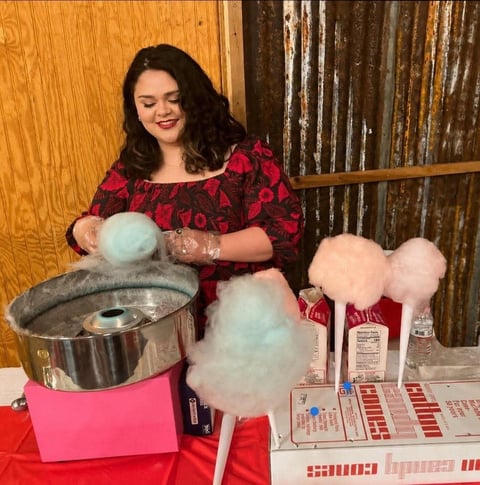 A team member in a red floral dress spinning fresh cotton candy at a Corner Stone event booth
